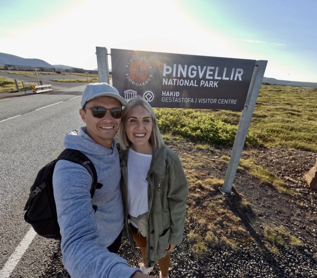 outsoorsy tourist couple posing in front of thingvellir national park sign golden circle iceland